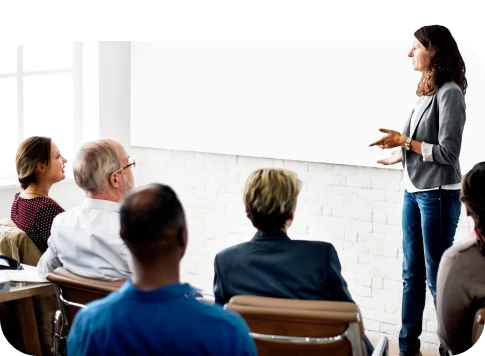 Homem de terno cinza e camisa branca fazendo palestra para um grupo de pessoas em ambiente de escritório moderno e bem iluminado.